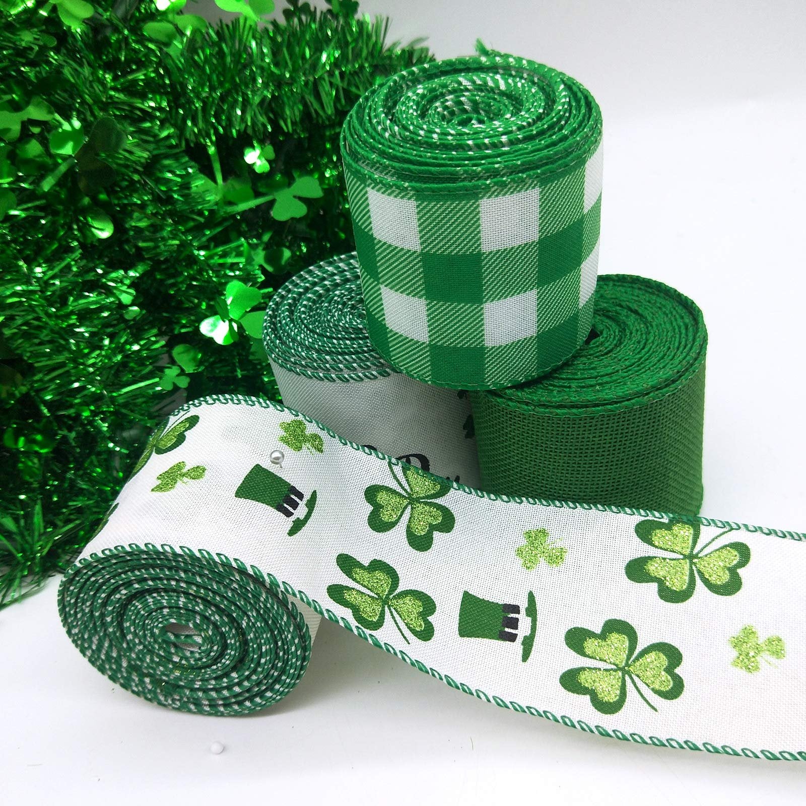 Four rolls of St. Patrick's Day themed ribbon with shamrocks and plaid patterns, arranged on a white background with green tinsel.