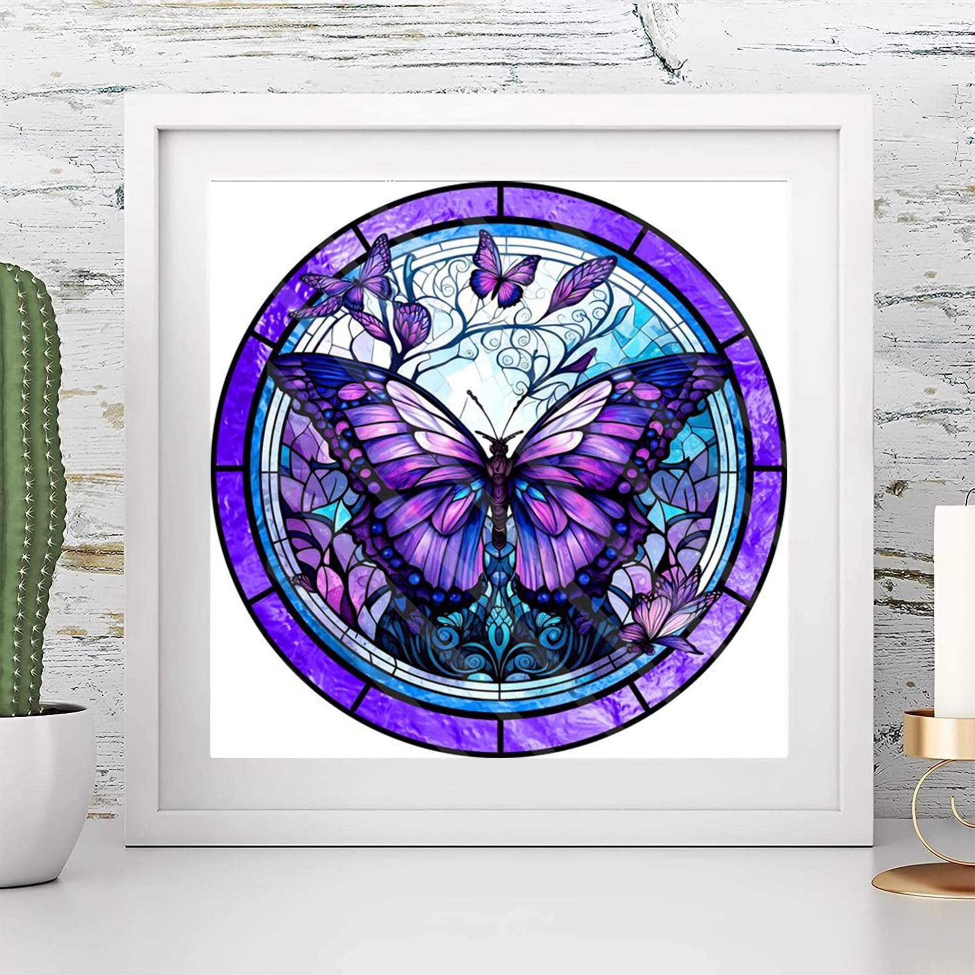 Stained glass butterfly diamond painting kit artwork framed on a white shelf with a cactus and candle holder.