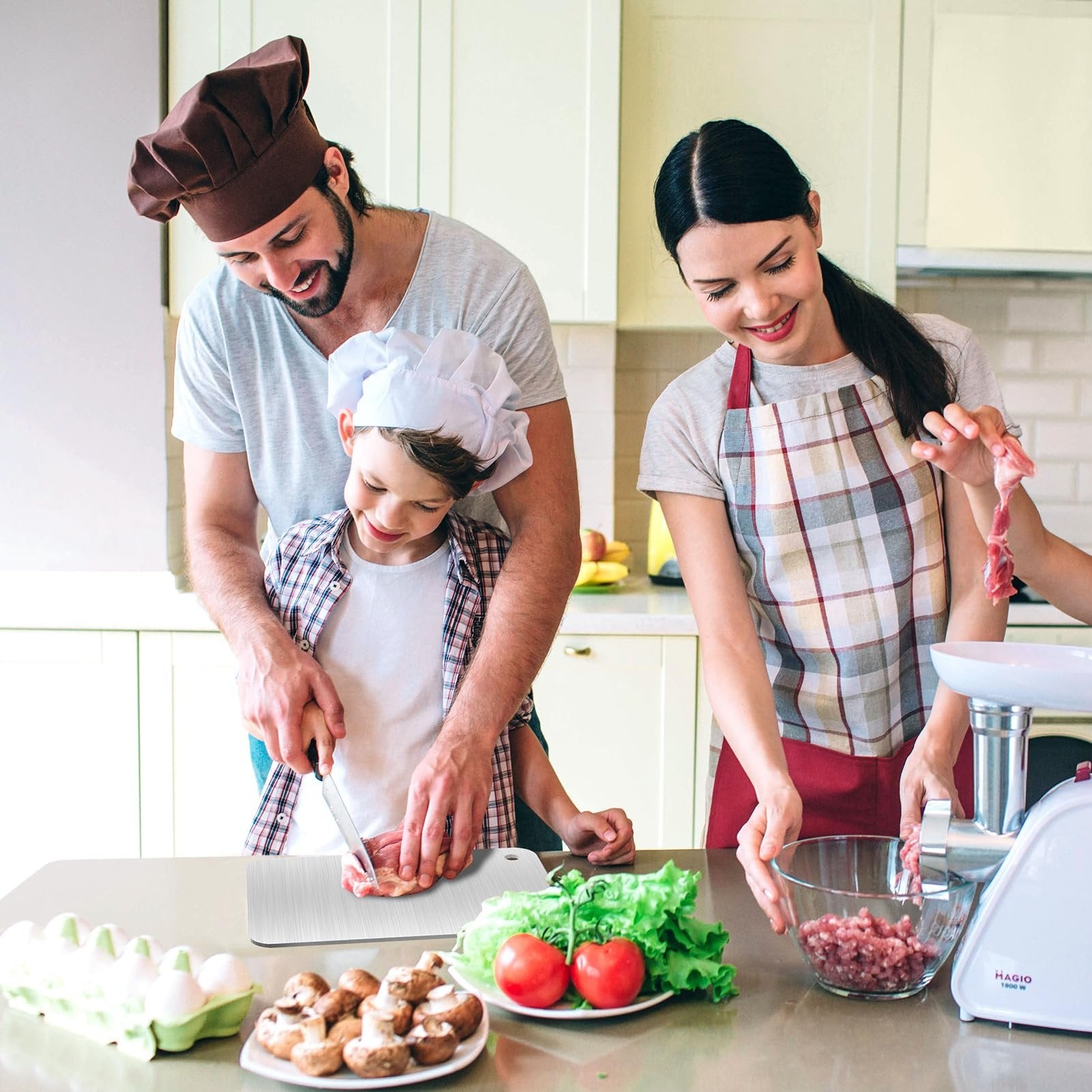 Family preparing food in kitchen, father and son cutting meat on stainless steel cutting board, mother using meat grinder.