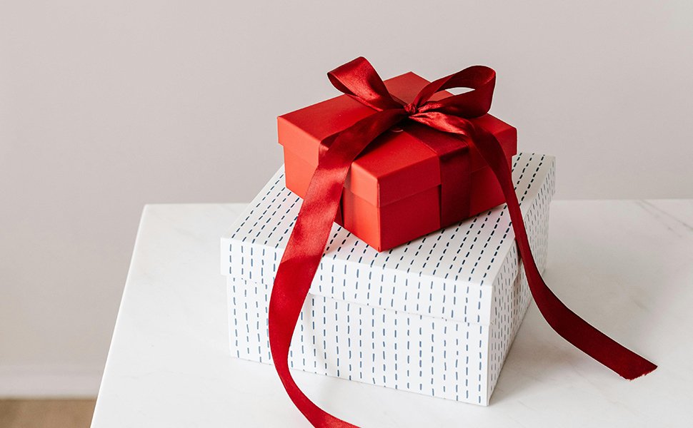Two gift boxes, one red and one white with blue dashes, stacked and tied with a red ribbon.