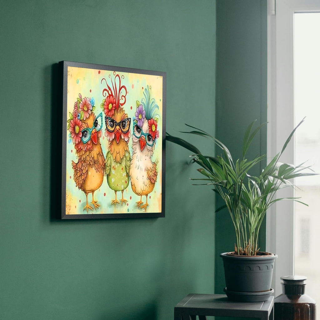 Framed stamped cross stitch art of three cartoon chickens wearing glasses and flower crowns hanging on a green wall.