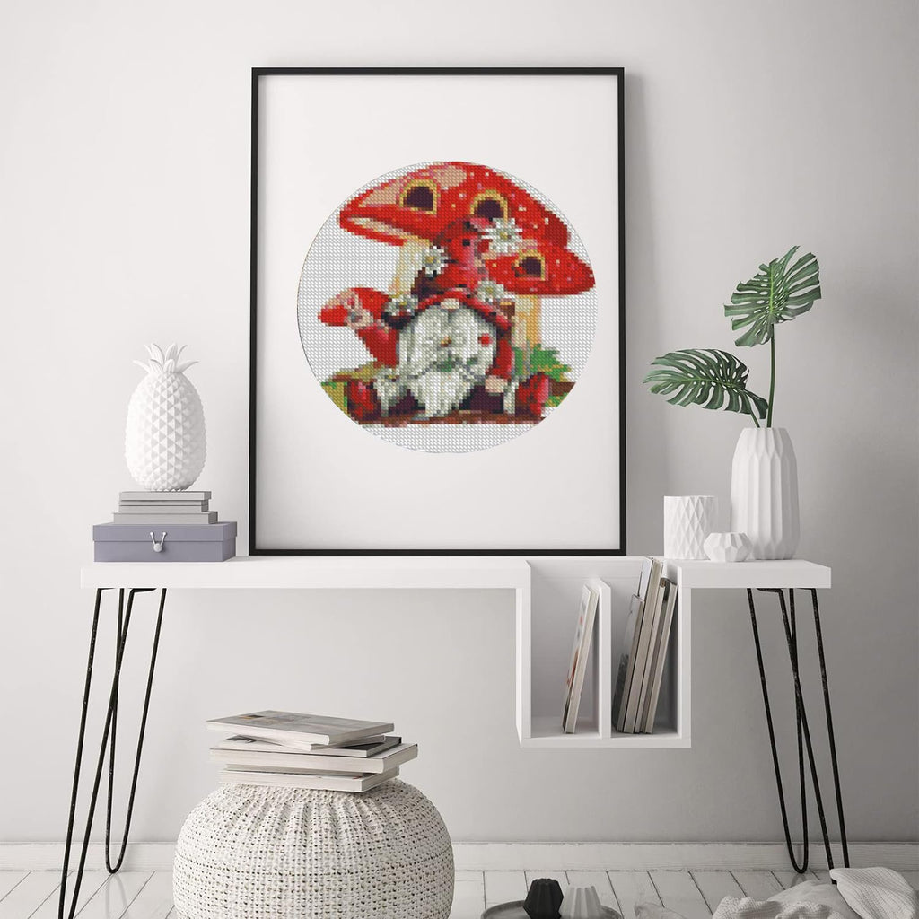 Stamped cross stitch kit featuring a gnome sitting on a mushroom, framed and displayed on a wall.