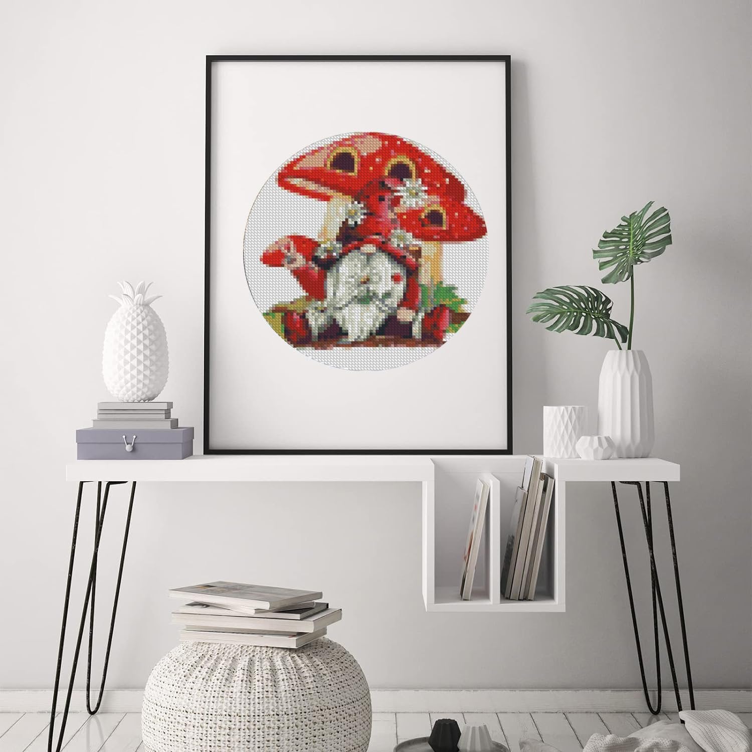 Stamped cross stitch kit featuring a gnome sitting on a mushroom, framed and displayed on a wall.