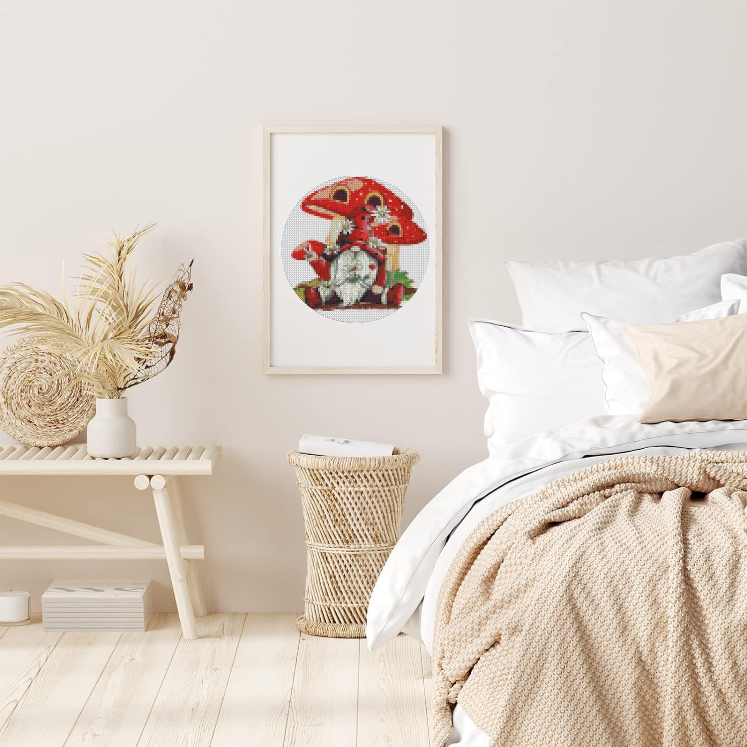 Framed cross stitch art of a gnome with mushrooms and strawberries hanging on a wall above a bench.