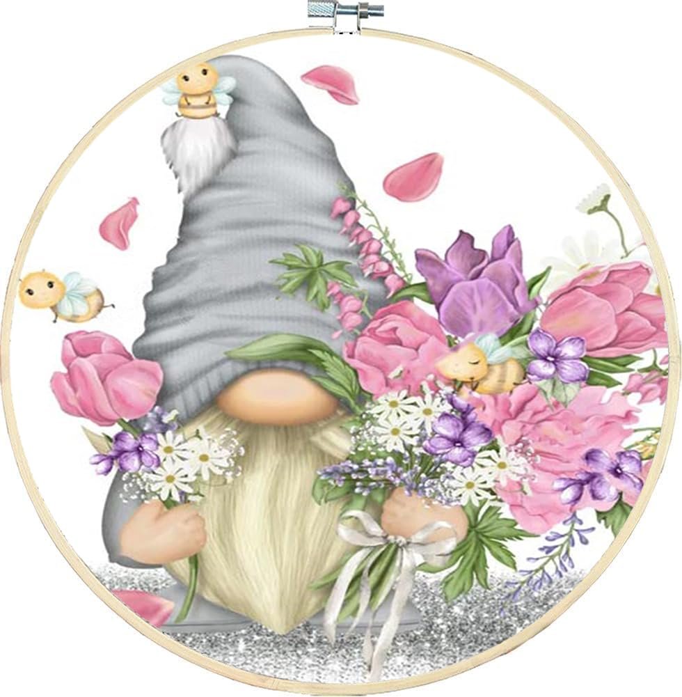 Stamped cross stitch kit featuring a gnome holding flowers and surrounded by bees and petals, within an embroidery hoop.