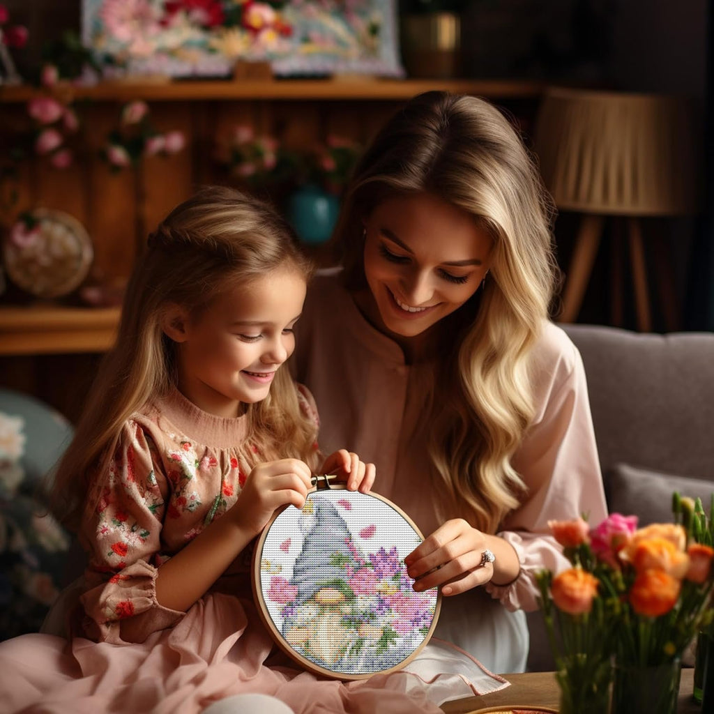 Mother and daughter smiling while doing cross stitch with gnome and flower pattern in embroidery hoop
