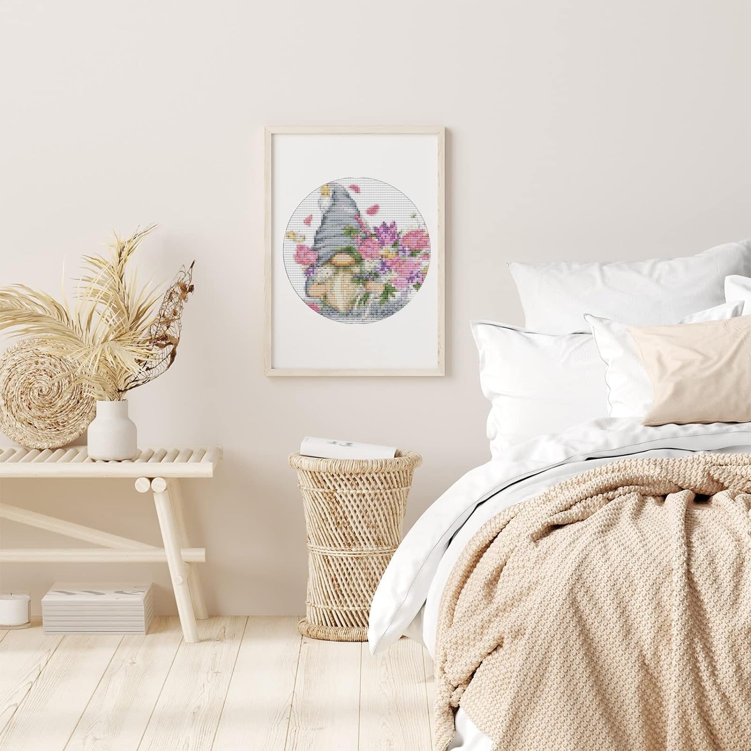 Framed stamped cross stitch art of a gnome with flowers hanging on a bedroom wall above a bench.