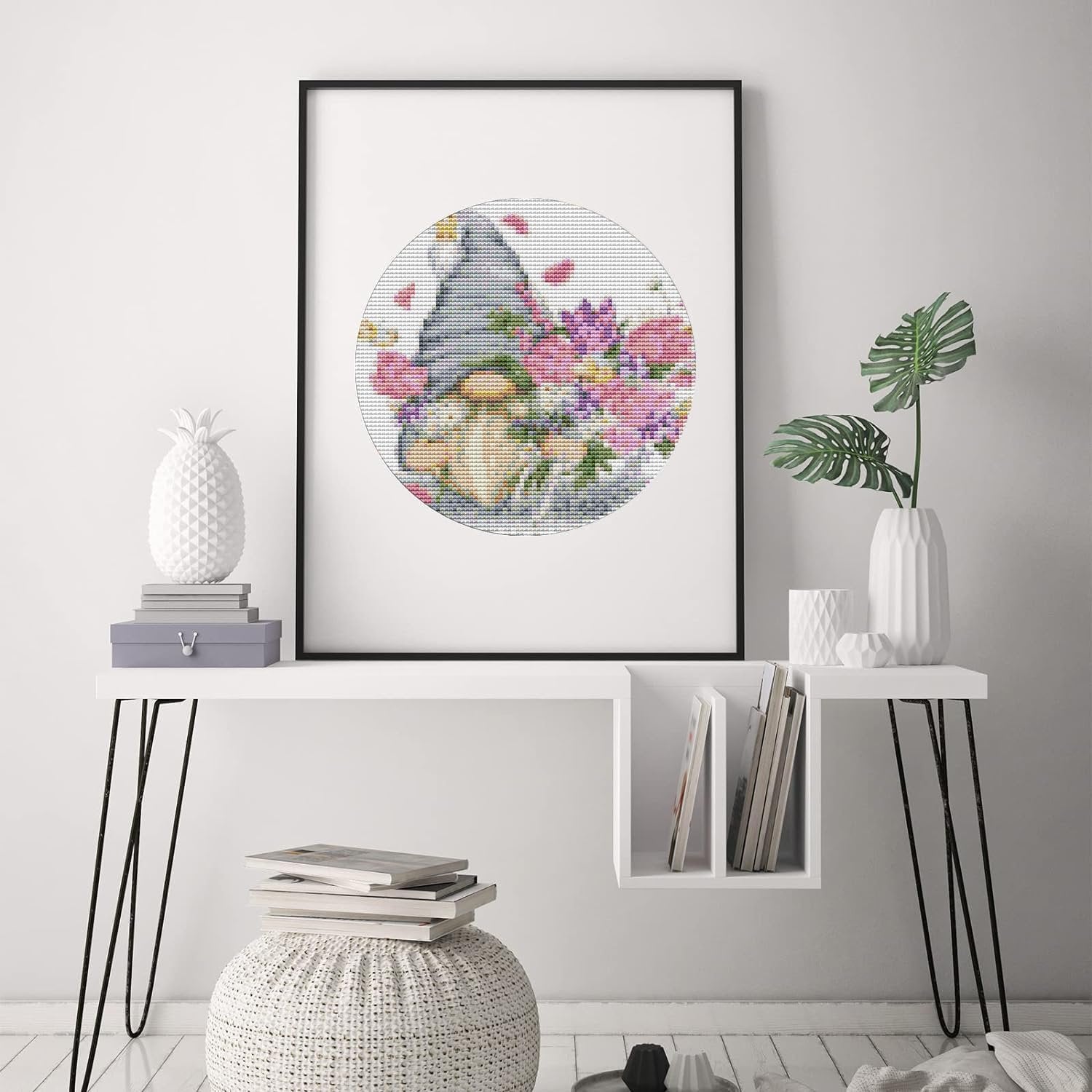 Framed stamped cross stitch kit with gnome and flowers pattern displayed on a wall.