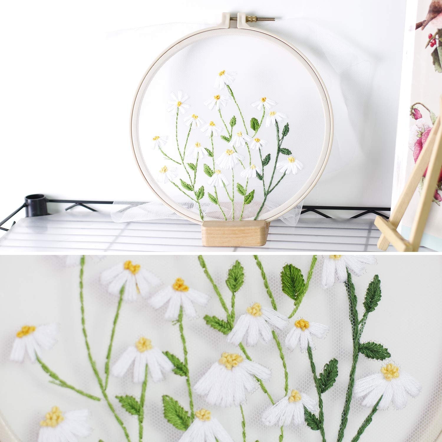 Embroidery hoop with white daisies and green stems stitched on white fabric, close-up view.