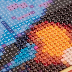 Close-up of a diamond painting kit showing colorful beads arranged on a grid with printed letters and numbers.