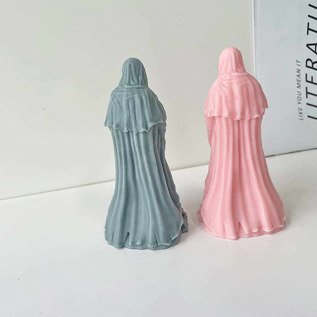 Two hooded figures, one grey and one pink, stand facing away from the camera on a white surface with a book in the background.