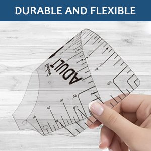 Clear plastic t-shirt ruler alignment tool with measurements, held by a hand against a wood-grain background.