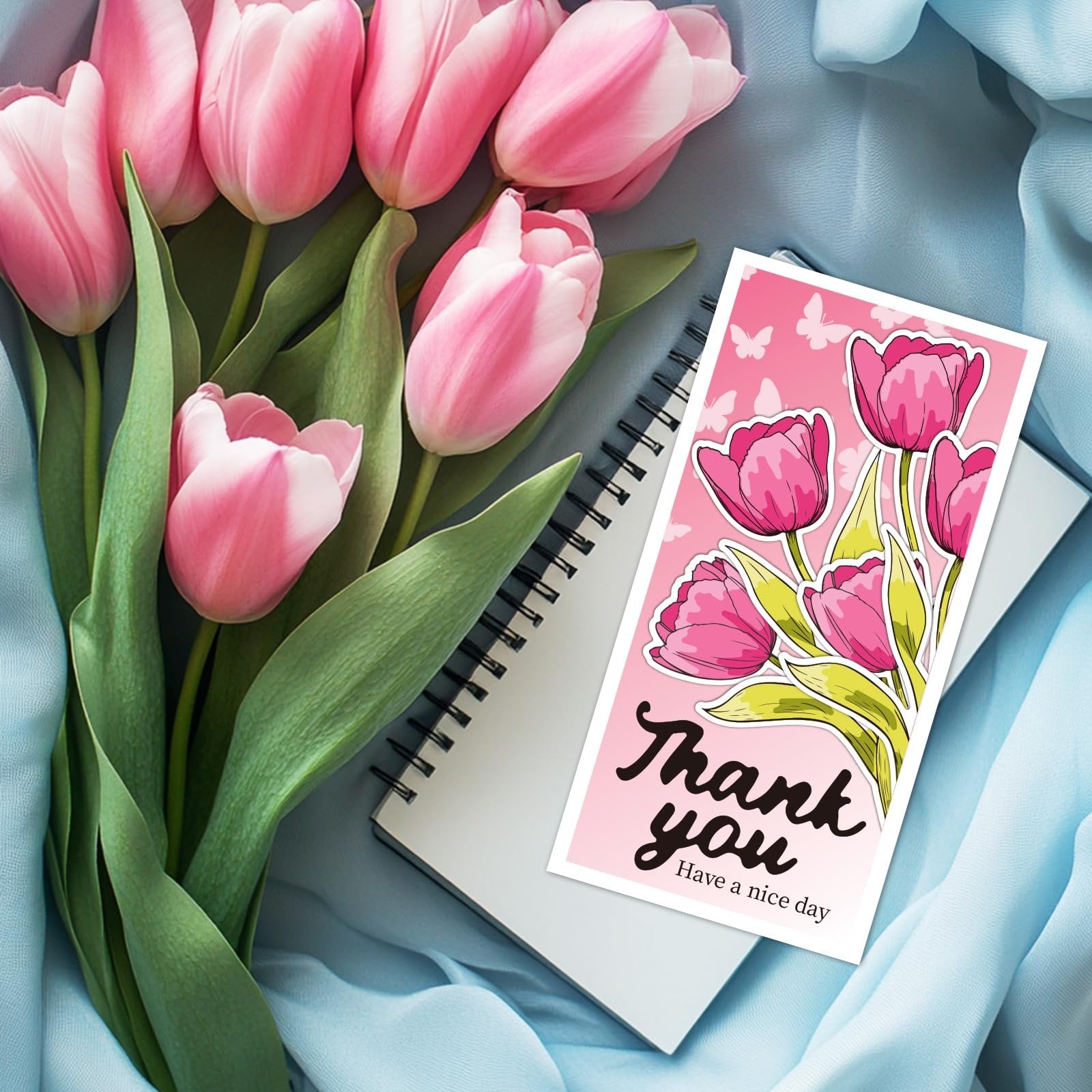 Pink tulips and a card with tulips and butterflies saying 'Thank you' on a blue cloth.