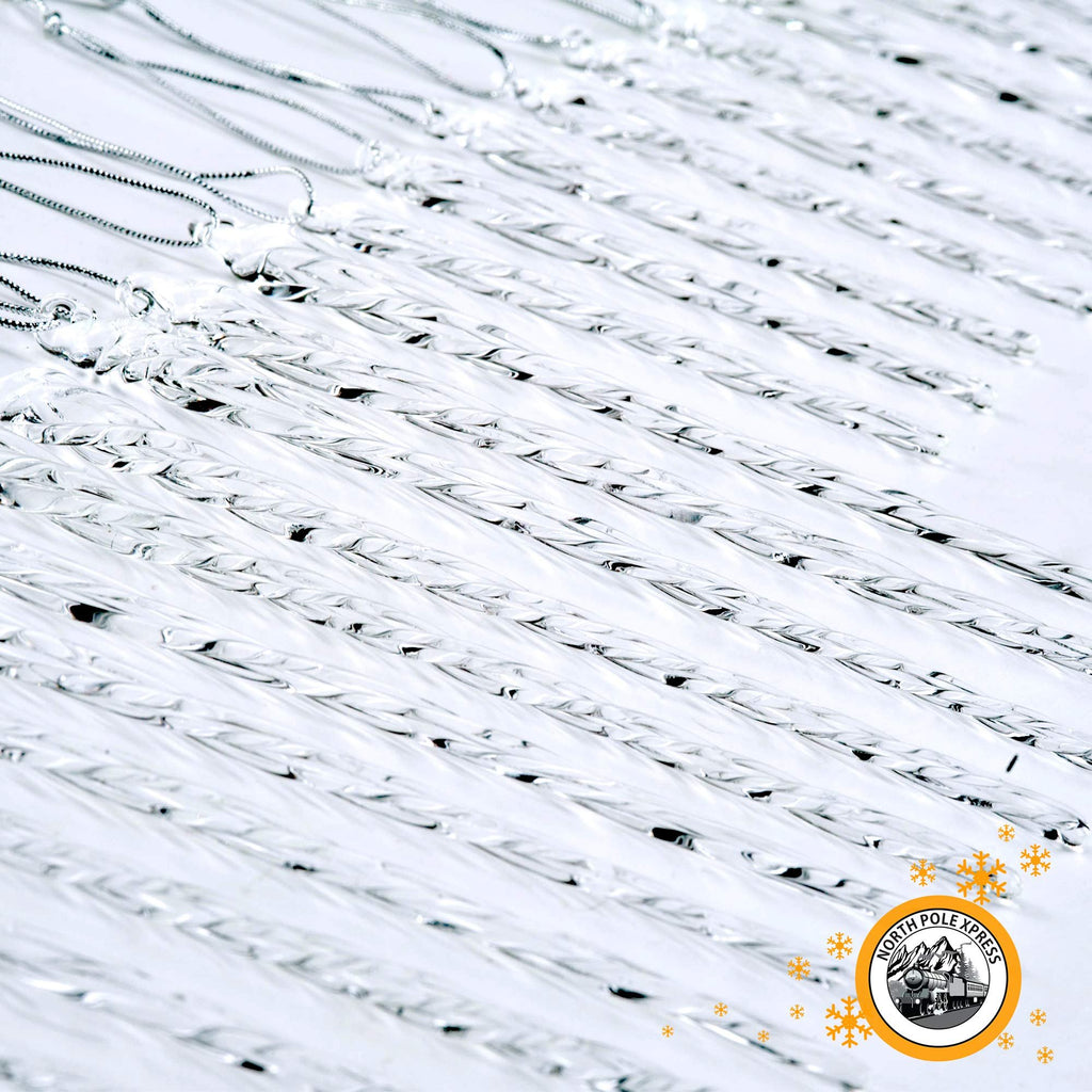 Close-up of multiple clear twisted glass icicle Christmas ornaments with silver cord hangers, arranged diagonally on a white background.