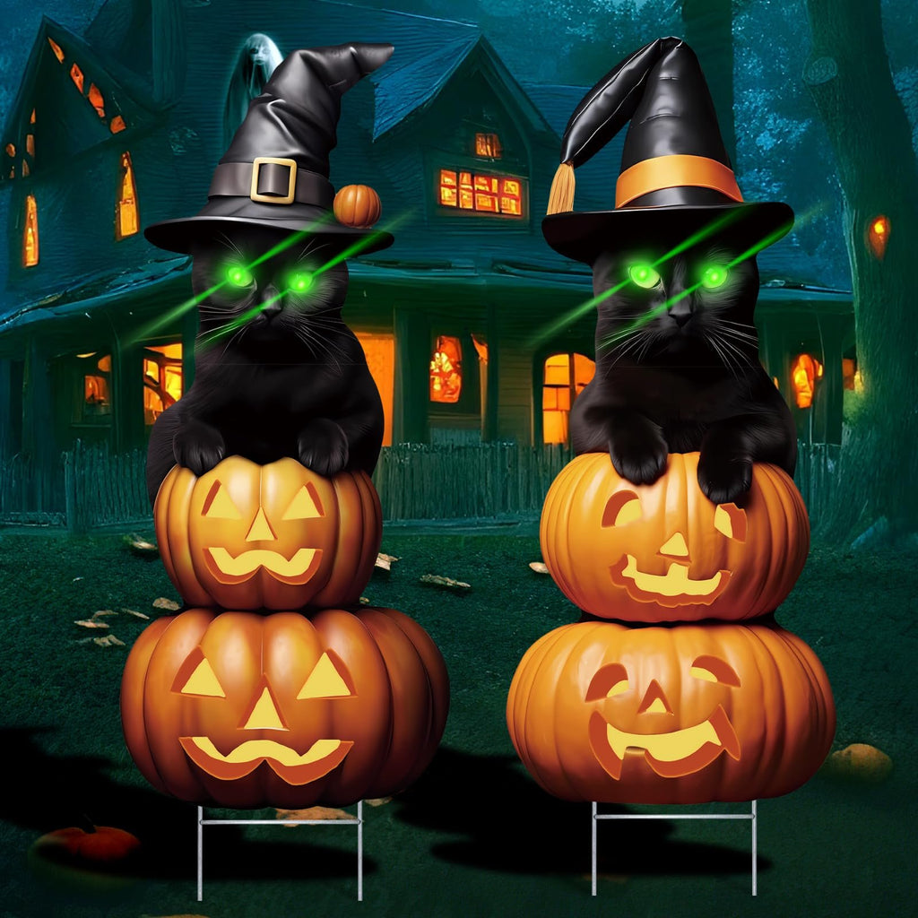 Two black cats wearing witch hats sit atop stacked jack-o'-lanterns in front of a haunted house, with green laser eyes.