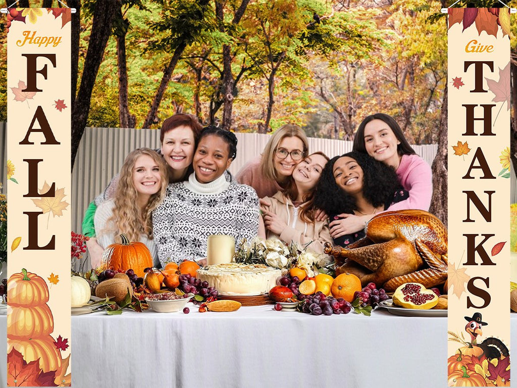 Group of smiling women posing behind a Thanksgiving feast, flanked by fall-themed porch banners reading 'Happy Fall' and 'Give Thanks'.