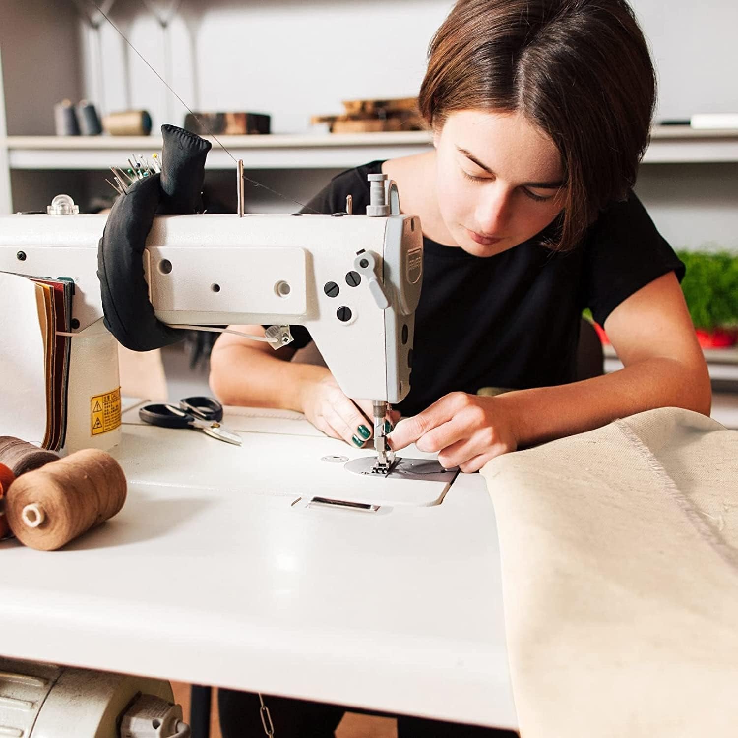 Woman sewing unbleached natural muslin fabric on a white sewing machine in a studio setting.