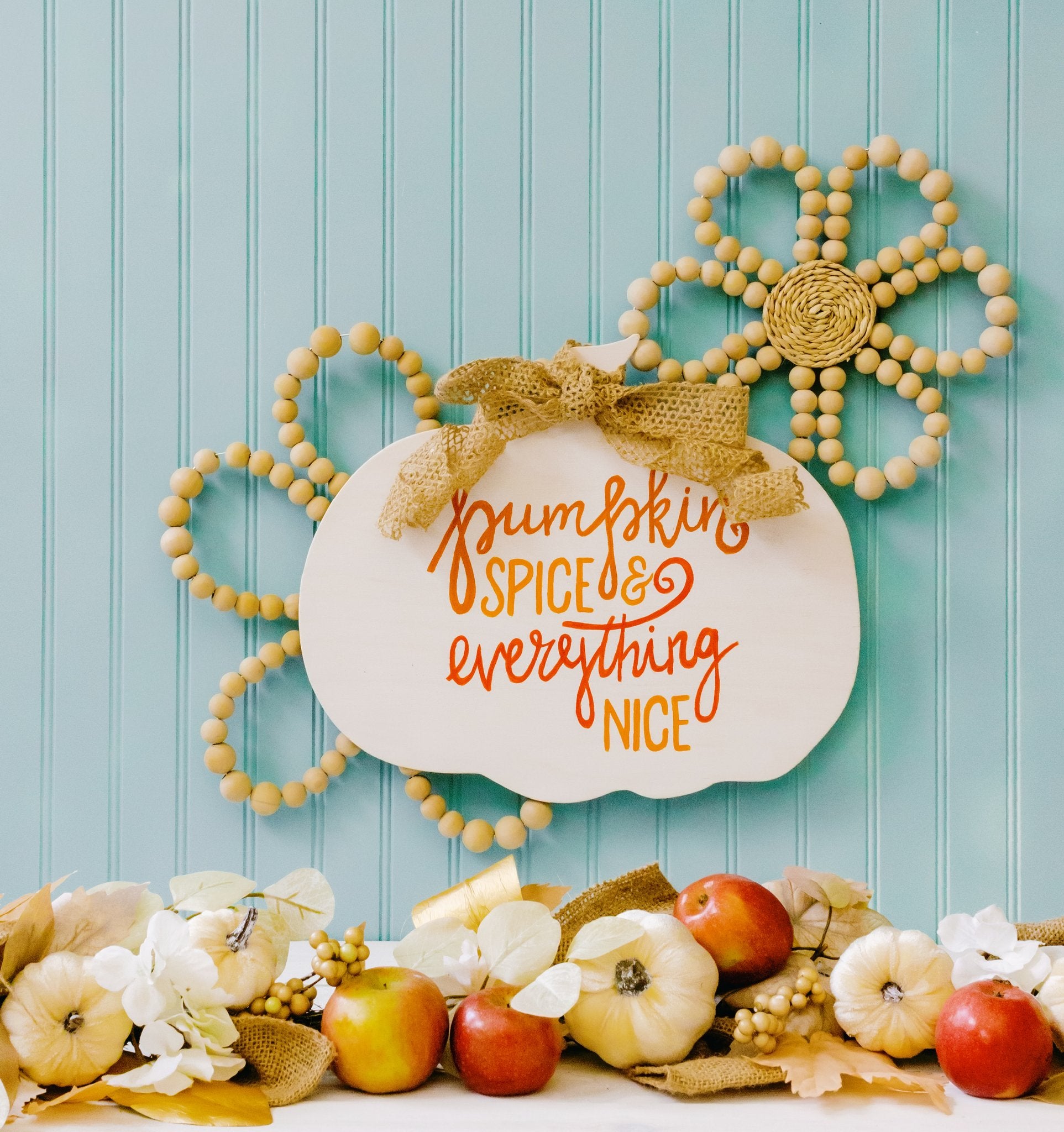 Unfinished plywood pumpkin cutout with 'Pumpkin Spice & Everything Nice' text, decorated with a burlap bow and surrounded by fall decor.