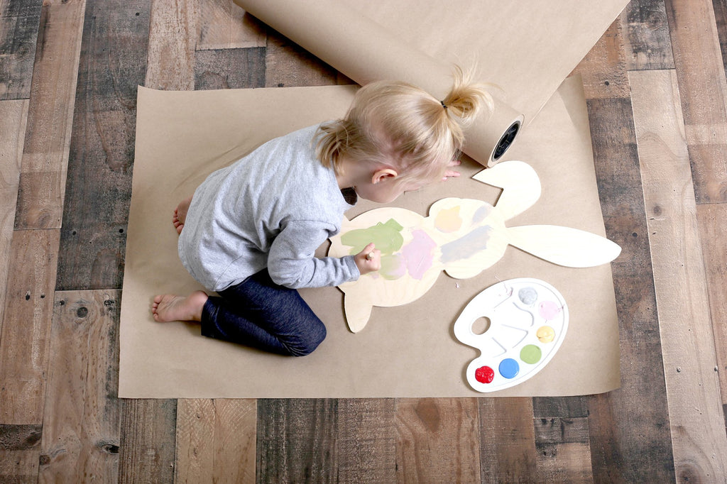 Toddler painting a wooden bunny cutout with pastel colors on kraft paper