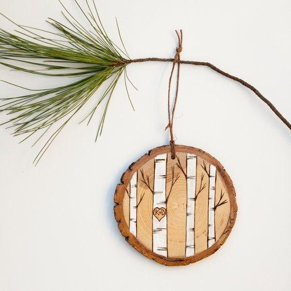 Round natural wood slice ornament with painted birch trees and a heart with initials K+D, hanging from a pine branch.