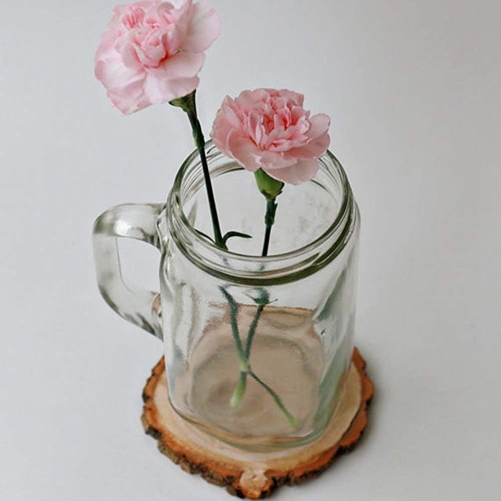 Unfinished natural pine wood slice with bark under a glass mason jar holding two pink carnations.