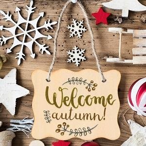 Wooden sign with 'Welcome autumn!' text and decorative branches, surrounded by craft supplies and holiday ornaments.