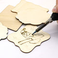 Hand using a wood burning tool on unfinished wood ornaments, creating a snowman design.