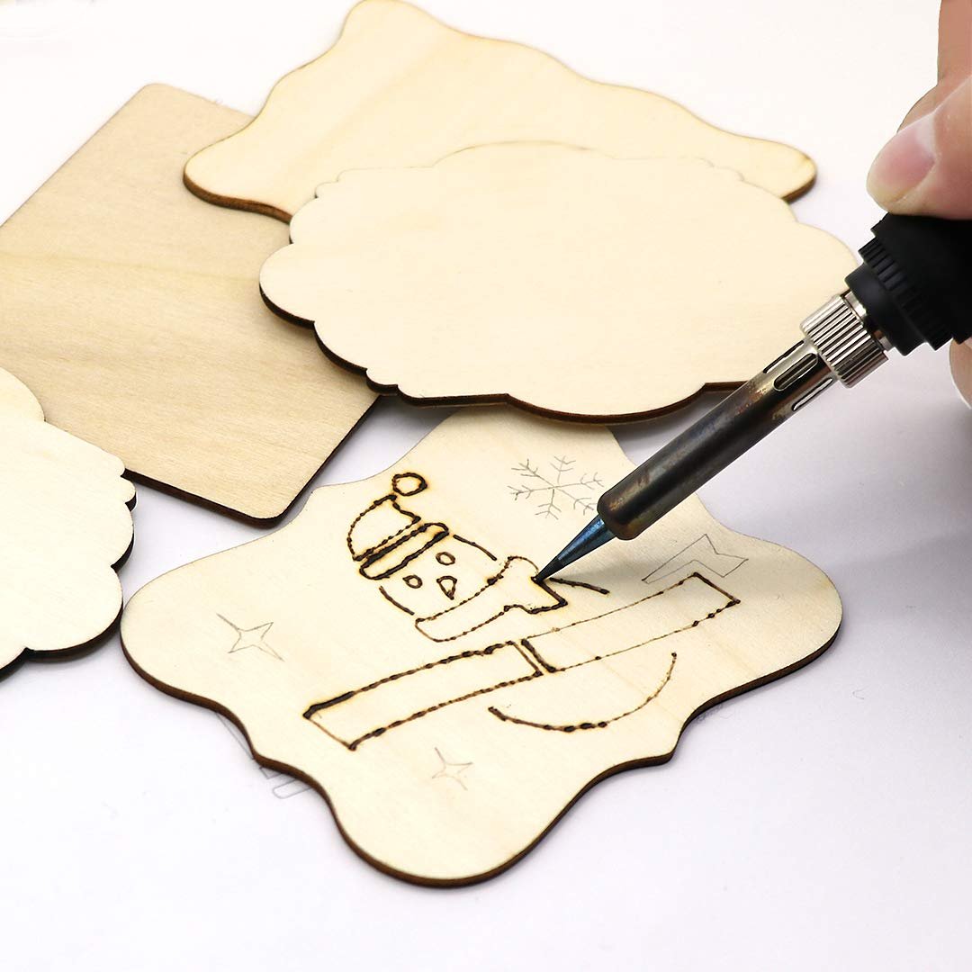 Hand using a wood burning tool on unfinished wood ornaments, creating a snowman design.