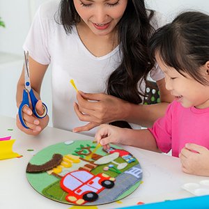 Mother and daughter crafting a felt scene on a round wooden base at a table