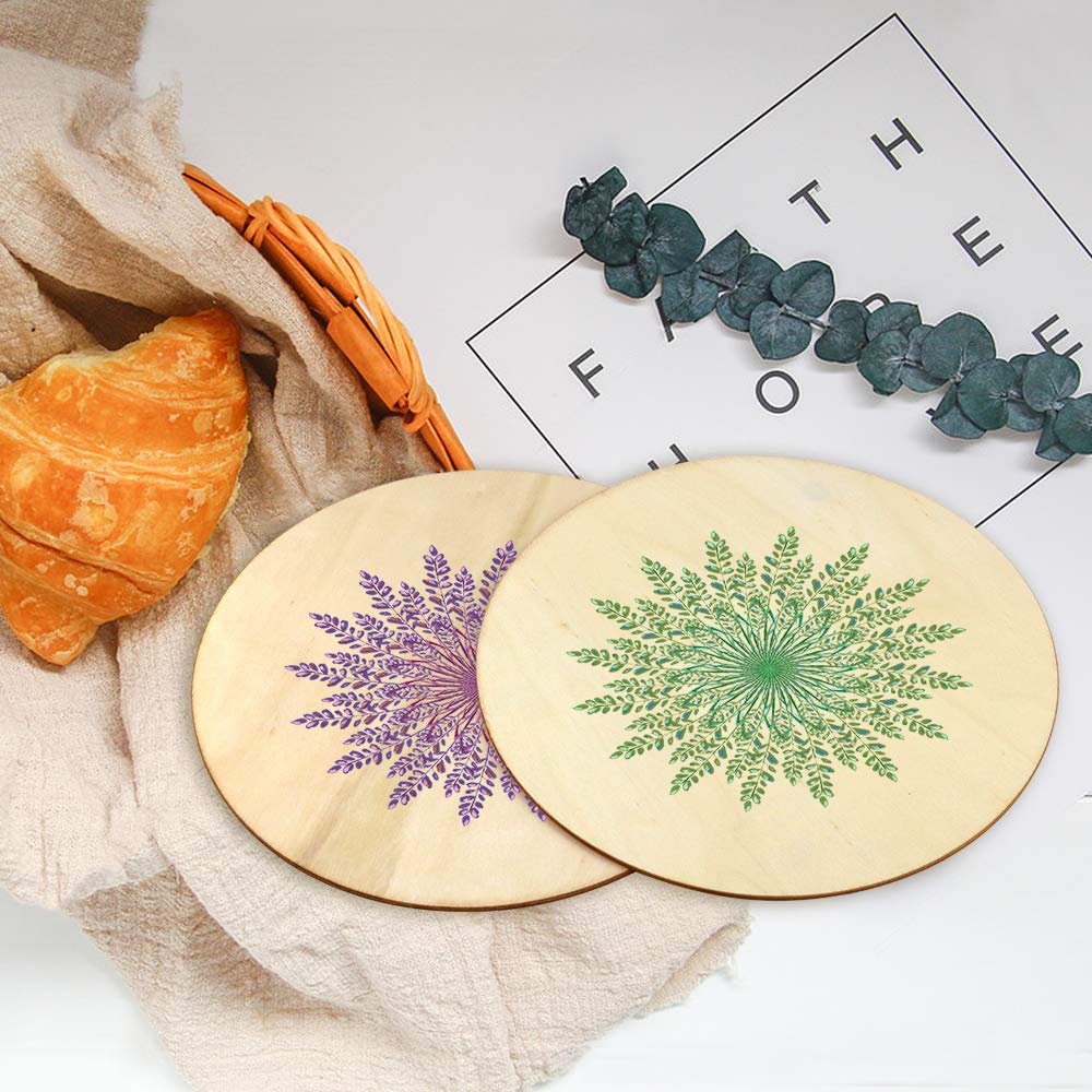 Two unfinished wood round circles with floral designs, one purple and one green, on a white surface with a croissant and greenery.