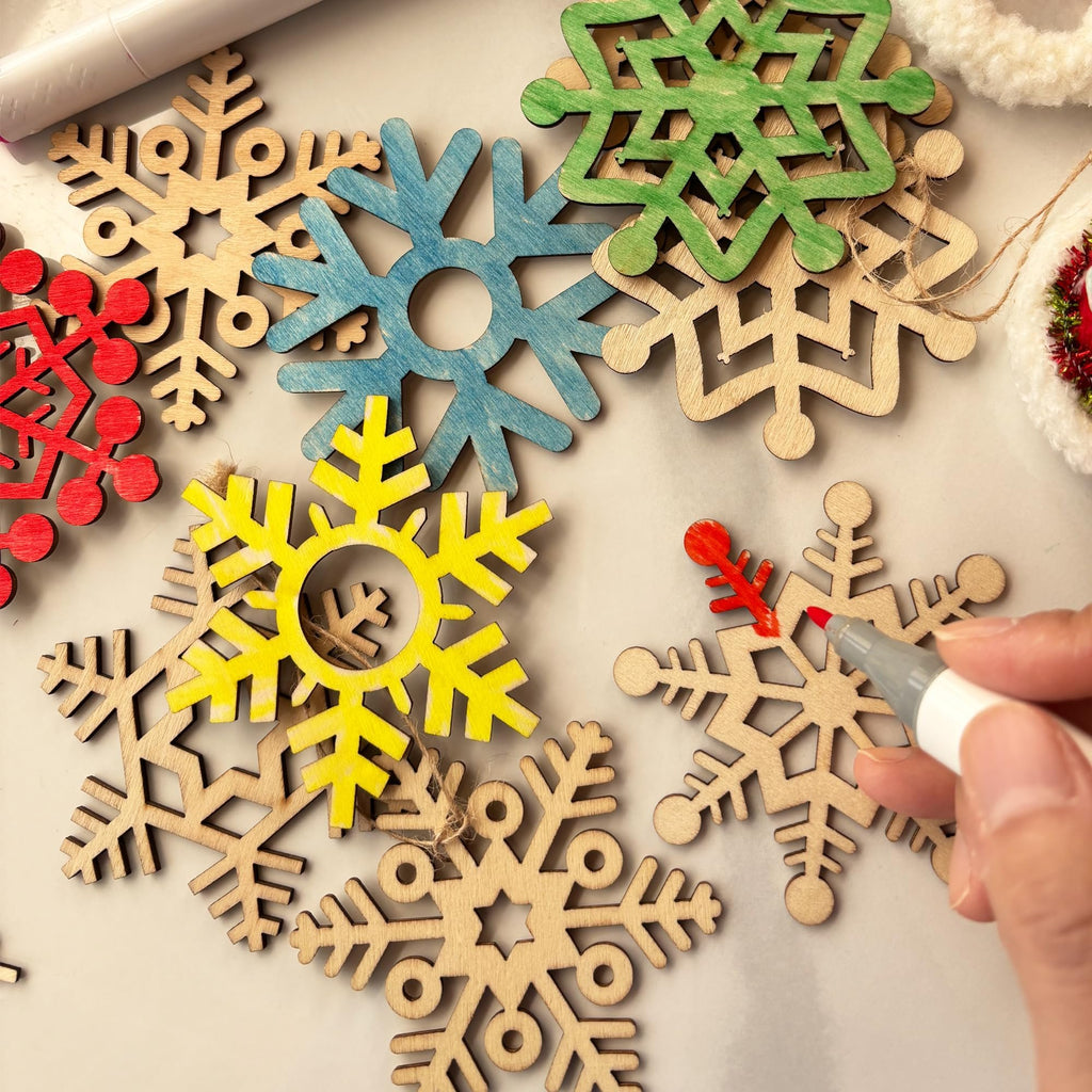 Hand coloring a wooden snowflake cutout with a red marker, surrounded by other unfinished and colored snowflake shapes.