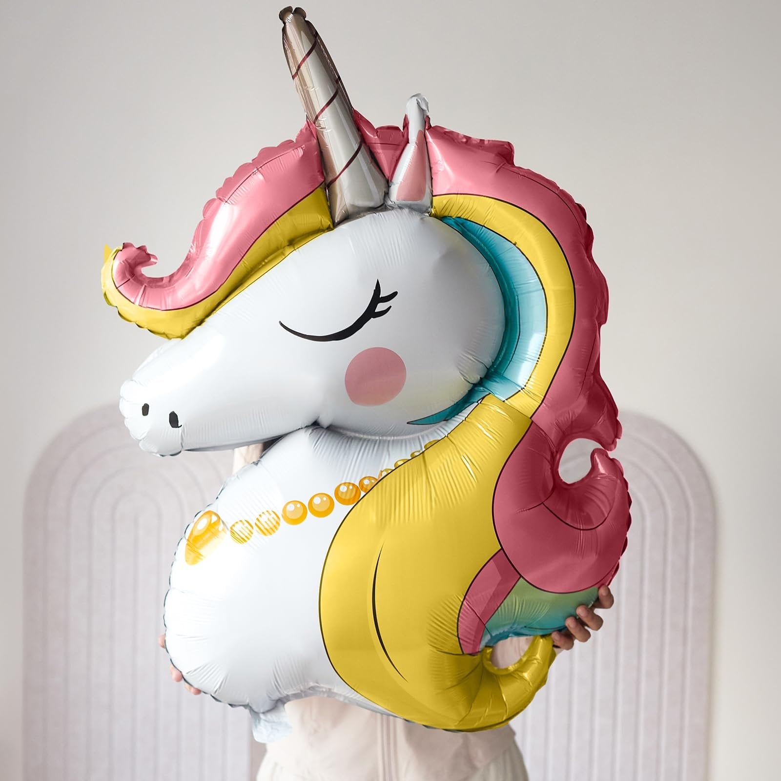 Person holding a large, colorful unicorn foil balloon with a pink mane and a pearl necklace detail.