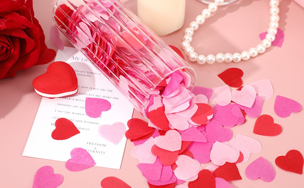 Valentine's Day heart confetti in red, rose, and pink spilling from a glass container, with a red rose, pearl necklace, and a card with text.