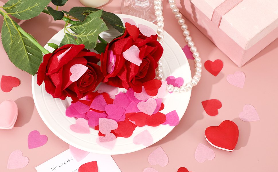 Two red roses with pink and red heart confetti on a white plate, surrounded by more confetti and a pearl necklace.