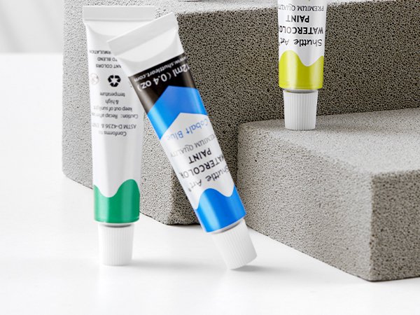 Three tubes of watercolor paint, one blue, one green, and one yellow, arranged on textured blocks.