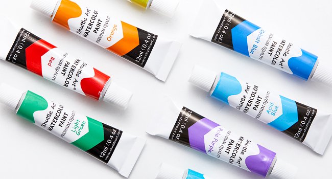 Assortment of watercolor paint tubes in various colors like red, orange, light green, pale purple, acid blue, and cobalt blue, arranged on a white surface.