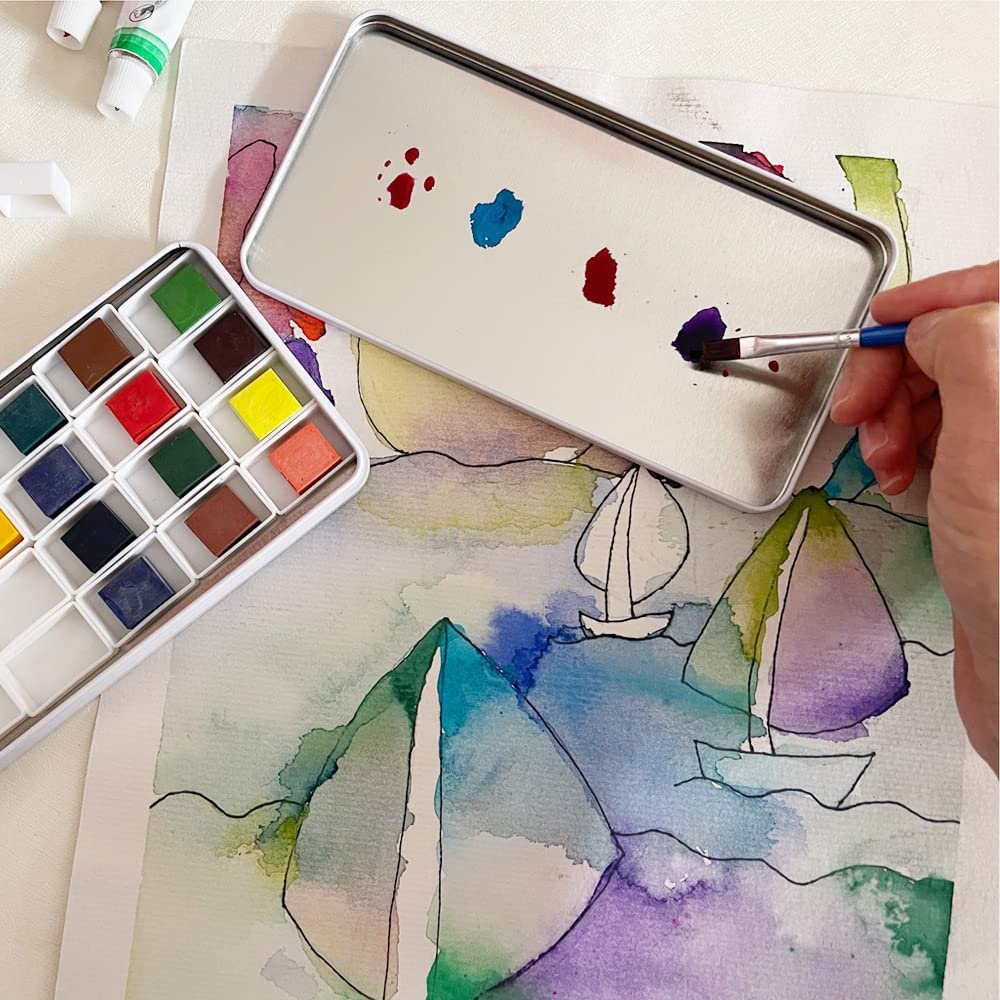 Watercolor palette tin box with colorful pans and a brush mixing paint on a painting of sailboats.