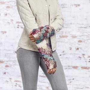 Woman wearing colorful knitted fingerless gloves with a quilted jacket and grey pants.