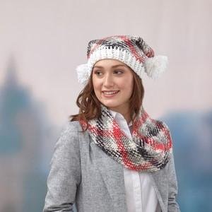 Woman wearing a knitted plaid hat with white pom-poms and a matching infinity scarf, styled with a gray blazer and white shirt.