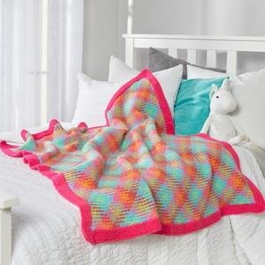 Crocheted blanket with pink trim draped on a bed with pillows and a stuffed unicorn