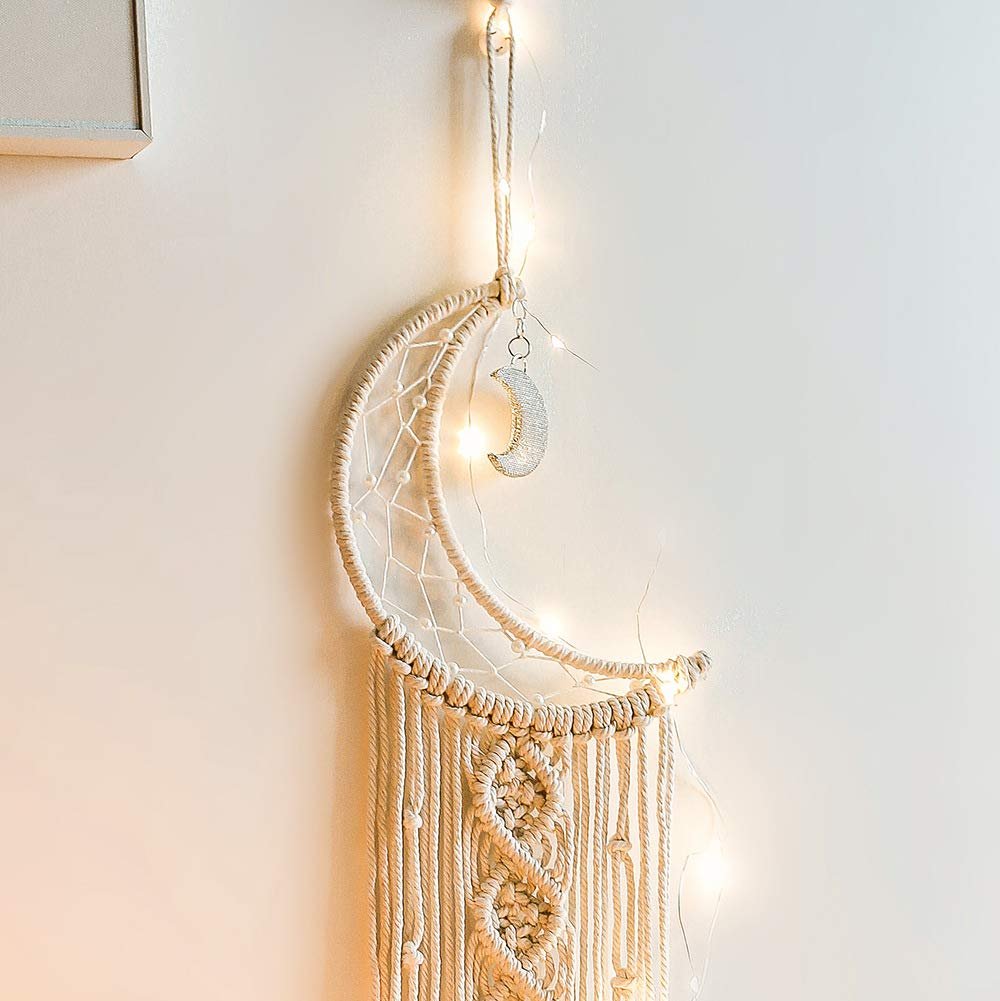 Macrame crescent moon dream catcher with string lights and a small moon charm hanging on a wall.