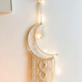 Macrame crescent moon dream catcher with string lights and a small moon charm hanging on a wall.