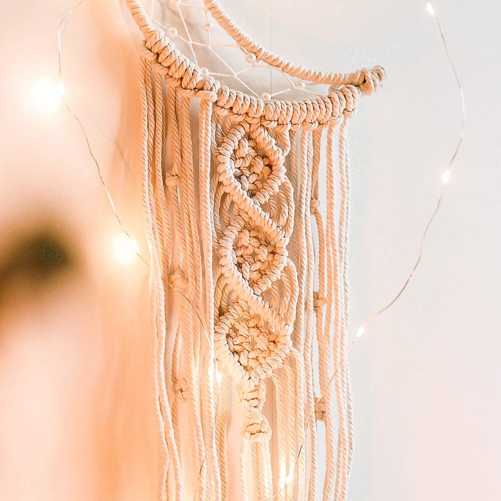 Macrame crescent moon dream catcher with intricate knotting and hanging tassels, adorned with fairy lights.