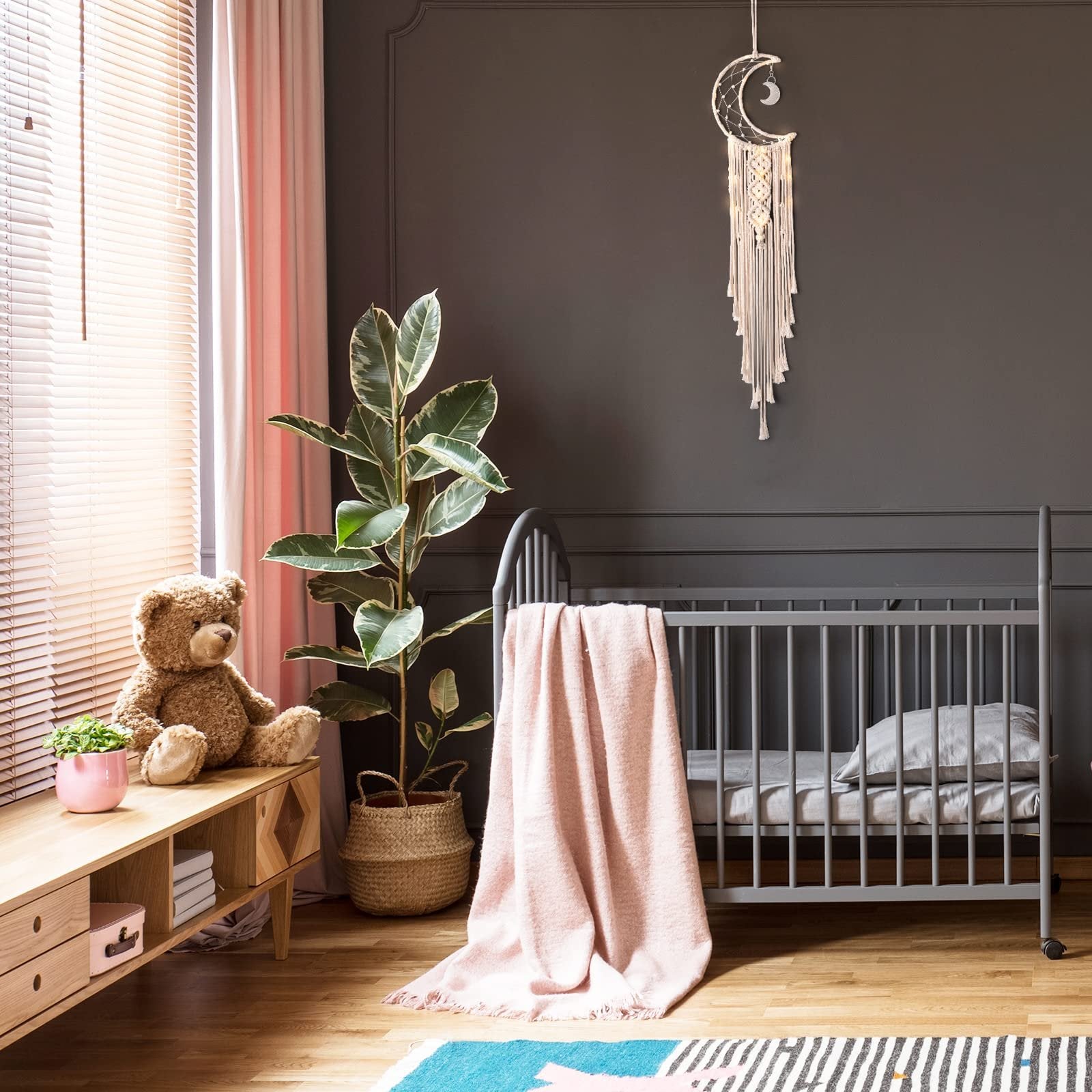 Macrame crescent moon dream catcher with string lights hanging above a crib in a nursery