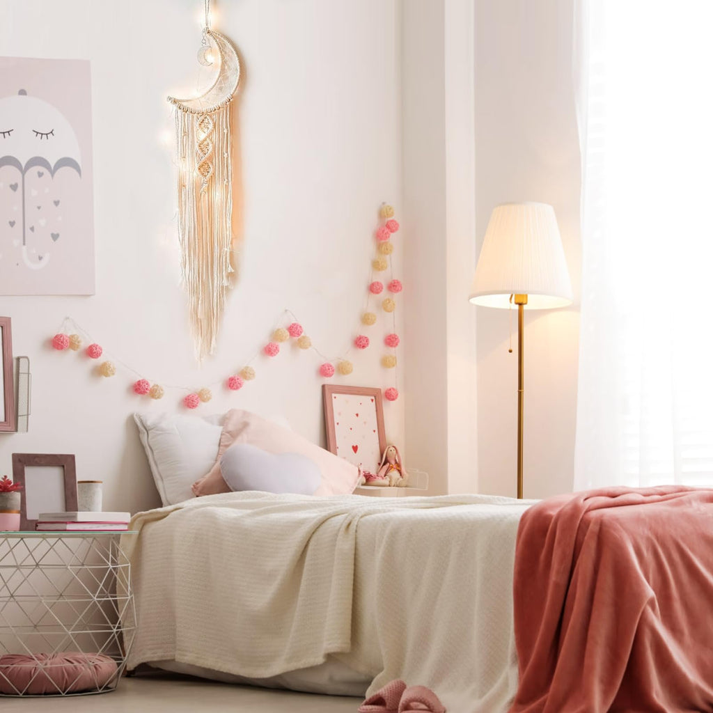 Macrame crescent moon dream catcher with string lights hanging above a bed in a bedroom setting.