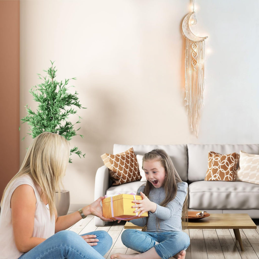 Mother giving a gift to her excited daughter in a living room with a macrame moon dream catcher on the wall