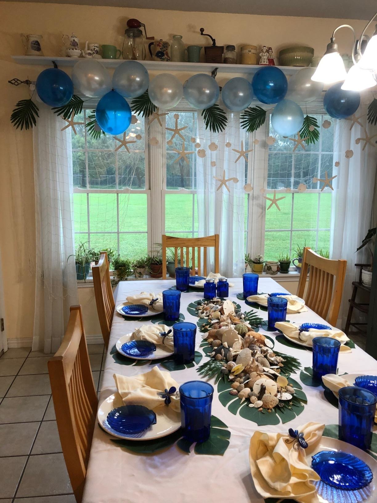 Dining table set for a nautical party with blue glasses, seashell plates, and a centerpiece of shells and starfish.