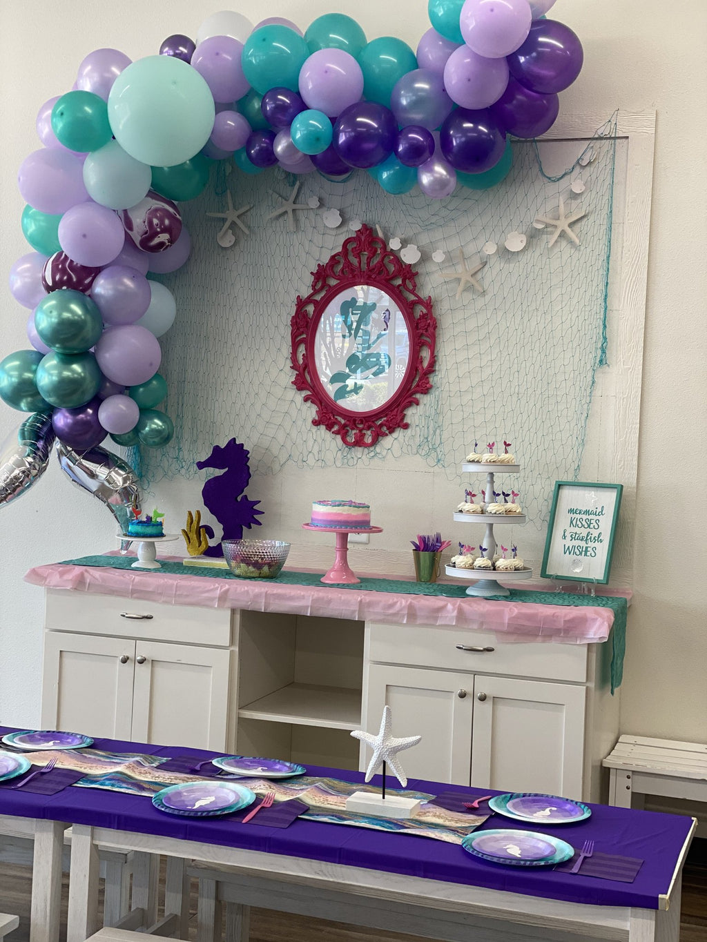 Nautical themed party table setting with purple tablecloth, plates, and napkins, cupcakes, and a cake.
