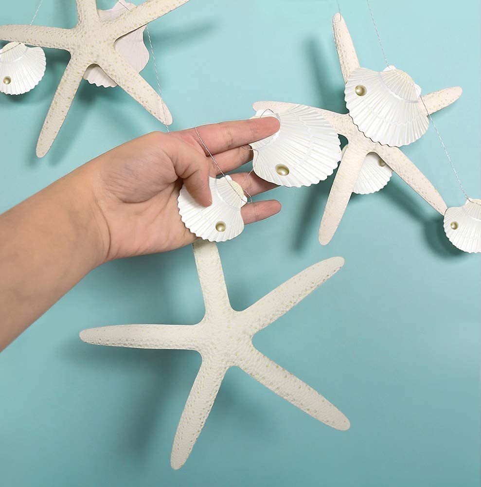 Hand holding a white paper garland with starfish and seashell cutouts against a teal background