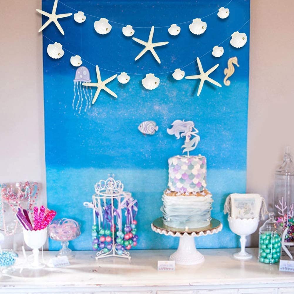 Seashell and starfish paper garland strung across a blue ocean backdrop with a cake and party decorations